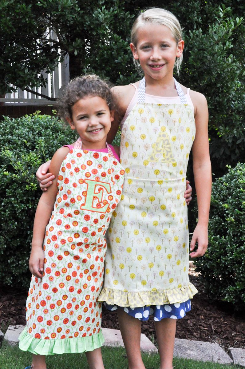 Two girls standing side by side wearing aprons.