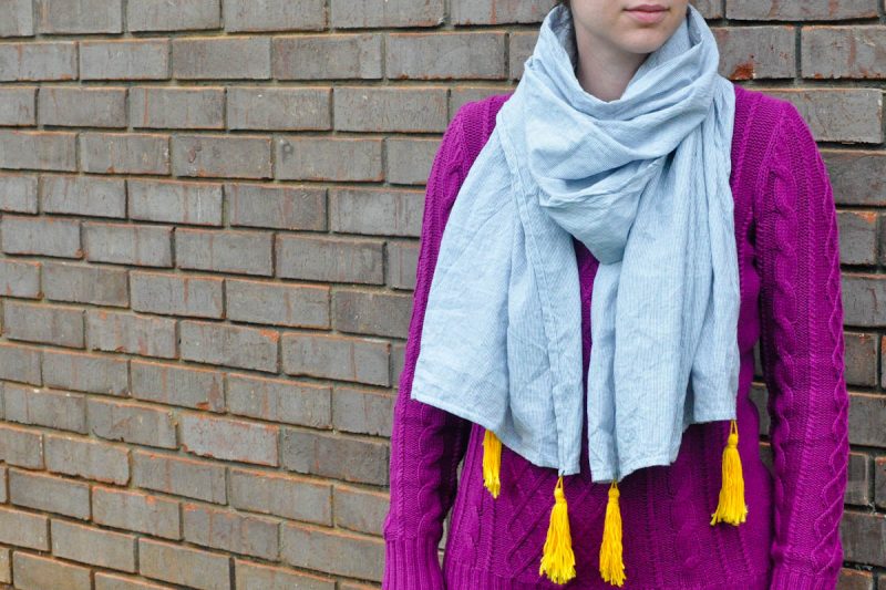 girl wearing scarf with tassels against brick wall