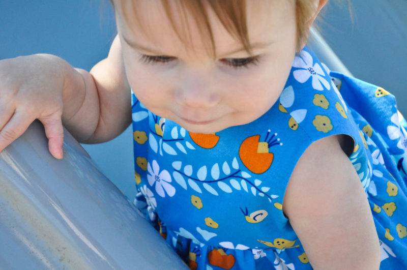 baby wearing blue dress will flowers on slide