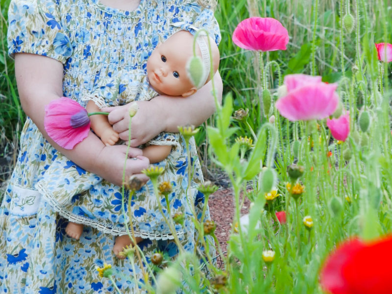 girl holding baby doll in flower garden