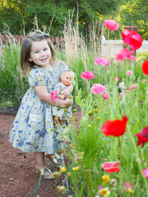 girl holding baby doll in flower garden