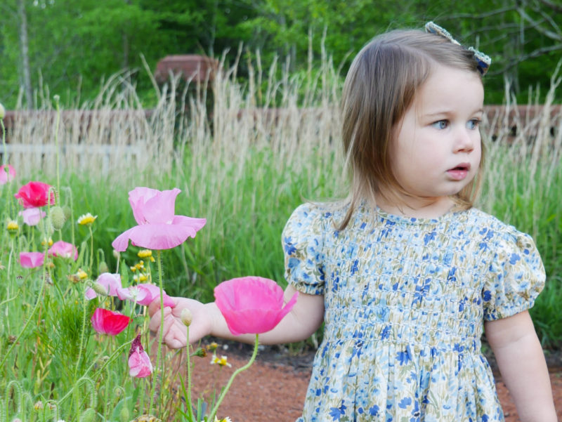 toddler wearing floral dress standing in garden